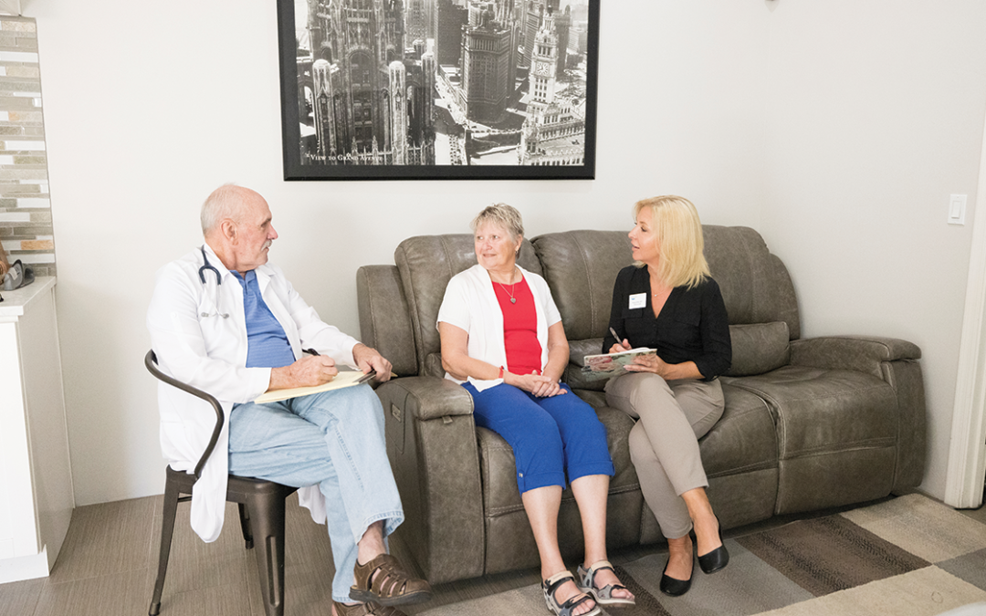 An elderly women sits on a couch alongside a representative from Your Patient's Advocate, discussing with a male doctor.